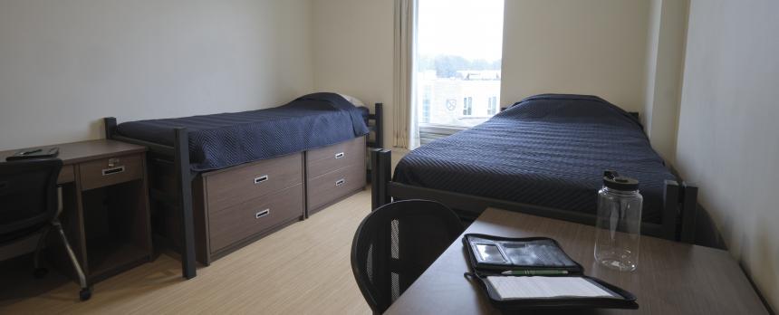 Residence room with two single beds, two desks and a window between the beds.
